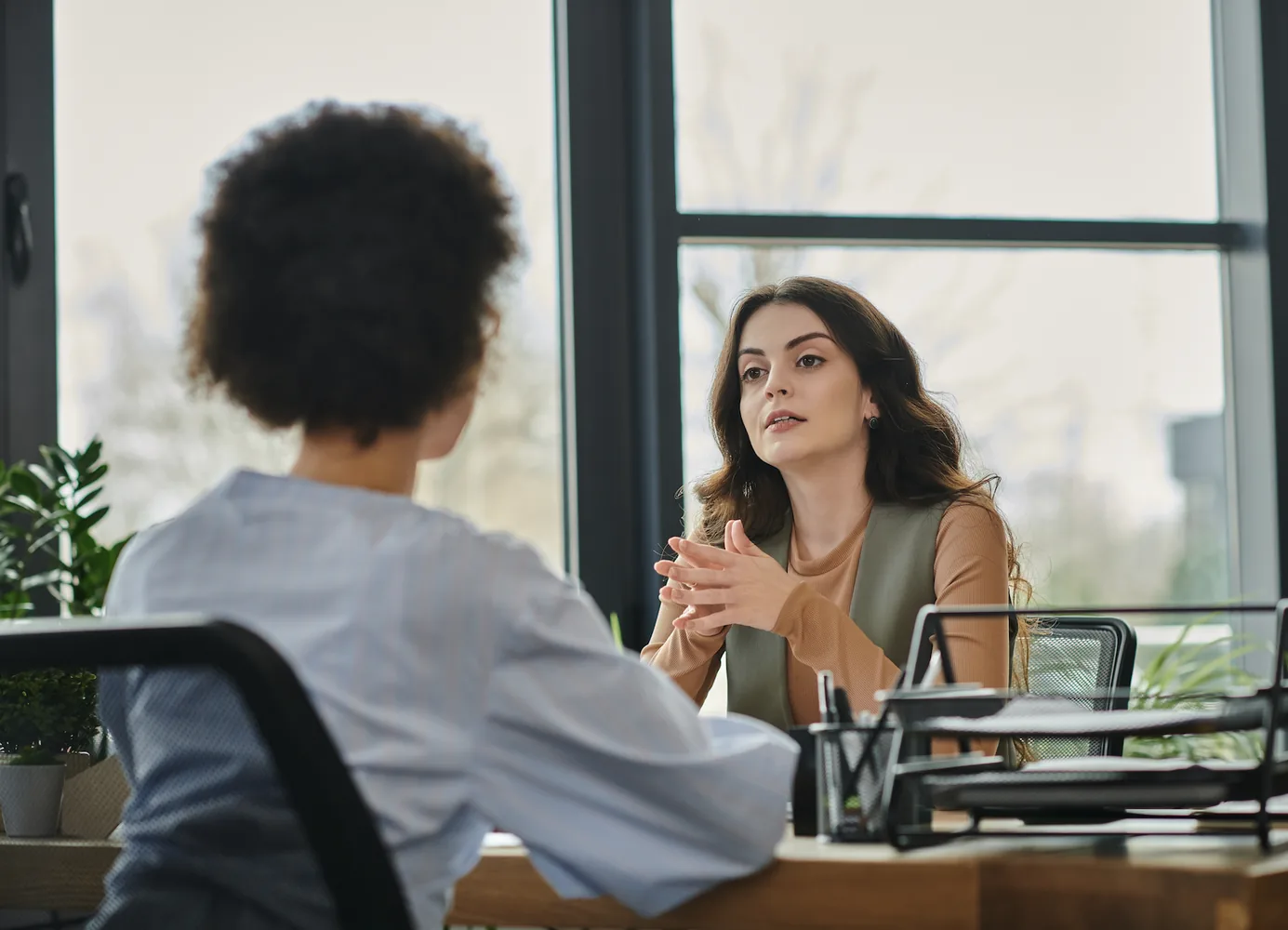Two women in a confidential conversation across a meeting table in an office.